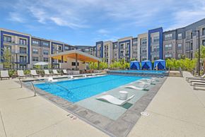 San Antonio apartment for rent - an outdoor pool with chairs and umbrellas and an apartment building in the background