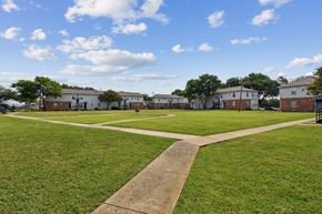 Dallas apartment for rent - A park with a pathway in the middle of a grassy area with buildings in the background.