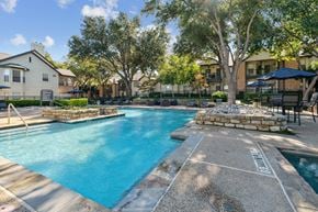 Grapevine apartment for rent - A swimming pool surrounded by trees and a stone border.