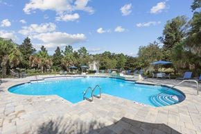 Saraland apartment for rent - A large swimming pool surrounded by trees and a clear blue sky.