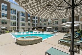 Carrollton apartment for rent - A large umbrella shades a pool area with lounge chairs.