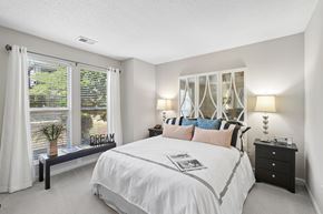 Cary apartment for rent - A bedroom with a large bed, a window with white curtains, and a nightstand with a lamp.