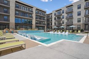 Lewisville apartment for rent - A swimming pool surrounded by sun loungers and umbrellas in front of apartment buildings.