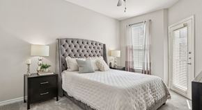 Dallas apartment for rent - A bedroom with a large bed, a nightstand with a lamp, and a window with curtains.