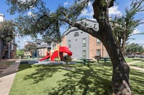 San Antonio apartment for rent - A playground with a red slide and a green bench is in front of a grey building.