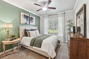 Dallas apartment for rent - A bedroom with a bed, a nightstand, a table, a lamp, a plant, and a mirror.