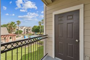 San Antonio apartment for rent - A balcony with a black railing and a brown door overlooks a pool and palm trees.