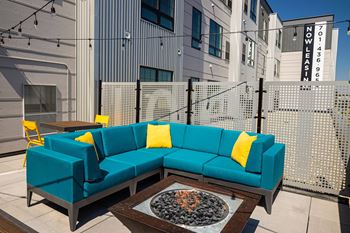 A seating area with a blue couch and yellow pillows in front of a building