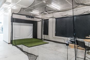 A batting cage in a room with nets and a table and chairs 