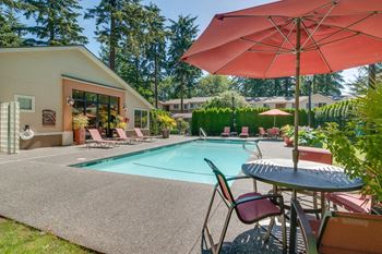 Swimming pool with lounge chairs and table with umbrella on a sunny patio