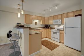 Anchorage apartment for rent - A spacious kitchen here at Admirals Cove with light brown cabinets, granite counter tops, bar type seating, and a ceramic sink. The room has a warm tone.