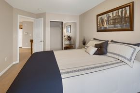 Anchorage apartment for rent - A bright bedroom at Admirals Cove featuring a neatly made bed with decorative pillows and patterned bedding. Soft beige walls and carpet create a warm feel. A sliding-door closet offers storage, and a doorway opens to the living area, giving the space an open, welcoming flow.