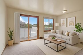 Anchorage apartment for rent - Bright living room at Arbor Pointe with a large beige sectional sofa, wooden coffee table, indoor plants, and sliding glass door leading to a balcony with views of nearby buildings and trees.