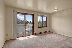 Anchorage apartment for rent - Empty living room at Arbor Pointe with beige carpet, a large sliding glass door leading to a balcony, an additional window allowing natural light, and cream-colored walls throughout