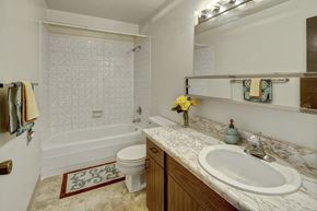 Anchorage apartment for rent - A clean bathroom at Arctic Sun Apartments featuring a bathtub and shower combo with tiled walls, a toilet, and a long marble-style countertop with a sink. A wide mirror with vanity lighting brightens the space, and towel racks and decor add color and warmth.