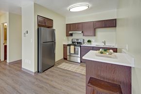 Anchorage apartment for rent - A modern kitchen here at Century Plaza featuring rich wood cabinetry, stainless-steel appliances, and a sleek breakfast bar with decorative accents. Light walls and wood-style flooring brighten the space, while ample counter areas and overhead storage create a clean, functional layout ideal for cooking and gathering.