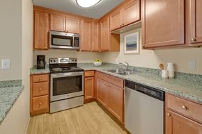 Anchorage apartment for rent - A warm, functional kitchen here at Club at Eagle Pointe featuring natural wood cabinetry, granite-style countertops, and stainless steel appliances including an oven, microwave, and dishwasher. Durable wood-style flooring and ample counter space create a practical layout that supports everyday cooking and comfortable meal preparation.