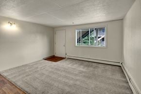 Anchorage apartment for rent - A bright, open living room here at College View featuring soft carpet flooring, neutral wall tones, and a large window that brings in natural light. The space includes a dedicated entry area, baseboard heating, and a flexible layout that easily accommodates seating and entertainment furniture for comfortable everyday living.