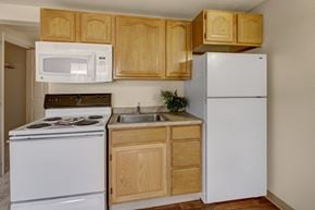 Anchorage apartment for rent - A clean, functional kitchen here at College View featuring classic wood cabinetry, white appliances, and a compact, efficient layout ideal for everyday cooking. The space includes a full-size refrigerator, electric range with overhead microwave, stainless sink, and durable countertops, offering practical storage and a bright, easy-to-maintain design.