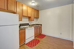 Anchorage apartment for rent - A functional kitchen here at Conifer Grove featuring warm wood cabinetry, laminate countertops, and a compact, efficient layout. White appliances include a full-size refrigerator, electric range, and sink, with wood-style flooring and overhead lighting providing a clean, practical space for everyday cooking.