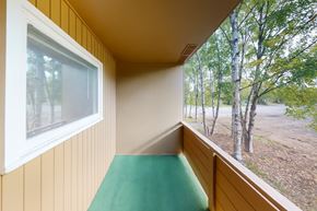 Anchorage apartment for rent - A covered balcony here at Country Lane offering a private outdoor space with neutral siding, sturdy railing, and a soft green floor surface, providing a peaceful spot to enjoy fresh air and views of surrounding trees while extending the apartment’s living space.