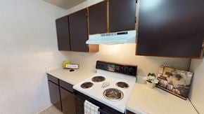 Anchorage apartment for rent - A functional kitchen here at Deer Park showcasing dark wood upper and lower cabinets, light countertops, an electric range with coil burners, a built-in vent hood, and simple decorative accents, with a clean, efficient layout designed for everyday cooking and convenient meal preparation.