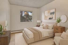 Anchorage apartment for rent - A cozy bedroom here at Deer Park featuring a neutral-toned upholstered bed with white bedding and a soft taupe throw, matching wood nightstands with lamps, modern abstract wall art, plush carpeting, and a window providing natural light for a calm, comfortable retreat.