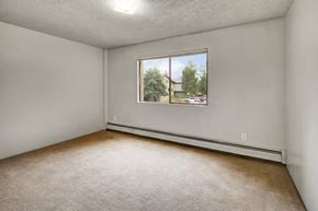 Anchorage apartment for rent - Airy bedroom here at Deer Park featuring wall-to-wall carpet, light neutral walls, and a large window that brings in natural light and outdoor views. A simple layout provides flexible space for bedroom furniture, while baseboard heating and an overhead light add everyday comfort and functionality.