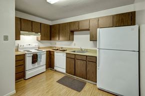 Anchorage apartment for rent - A bright kitchen here at Driftwood featuring warm wood cabinetry, generous laminate countertops, a white refrigerator, electric range with vent hood, built-in dishwasher, stainless sink, and wood-style flooring, creating a clean, functional space designed for comfortable everyday cooking and easy meal preparation.