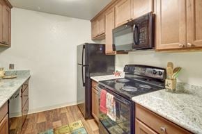 Anchorage apartment for rent - A compact kitchen here at Hillside Chalet, with a black stove top oven and a black refrigerator. Includes soft wooden cabinets and drawers.