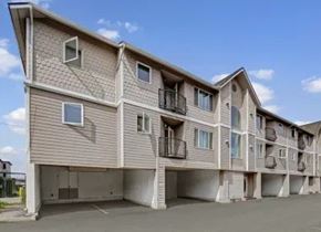 Anchorage apartment for rent - Three-story apartment building here at La Maisonnette with beige siding and white trim. The building features private balconies, covered parking beneath the structure, and multiple exterior windows in a residential setting.