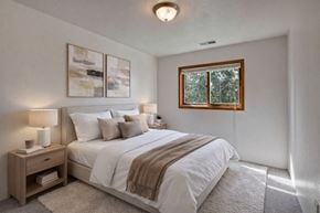 Anchorage apartment for rent - A bedroom with a large bed, a nightstand with a lamp, and a window with a view of trees.