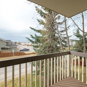 Anchorage apartment for rent - A covered balcony at Legacy West with a railing overlooking nearby trees, neighborhood buildings, and a quiet street view.