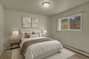 Anchorage apartment for rent - A cozy bedroom here at Montclair with a queen bed dressed in white bedding, neutral pillows, and a taupe throw blanket, paired with matching nightstands and soft bedside lamps.