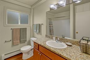 Anchorage apartment for rent - A clean bathroom here at Montclair with a wood vanity, speckled granite-style countertop, and a large mirror above a white sink.