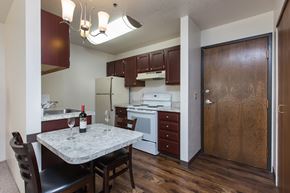 Anchorage apartment for rent - A clean compact kitchen here at Outlook with dark wood cabinets, light countertops, and white appliances, featuring a small dining table under warm overhead lighting, creating a cozy dining and kitchen space.