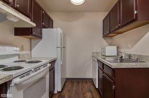 Anchorage apartment for rent - A compact kitchen here at Outlook with dark wood cabinets, light countertops, and white appliances, including a stove, refrigerator, dishwasher, and stainless steel sink.