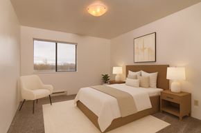 Anchorage apartment for rent - A serene bedroom here at Outlook with a wood-framed bed, crisp white bedding, matching nightstands with modern lamps, and a cozy accent chair beside a large window with peaceful views.