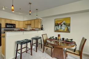 Anchorage apartment for rent - A stylish dining area here at Park Plaza II with a round wooden table and upholstered chairs, featuring a granite breakfast bar with barstool seating, light wood kitchen cabinets, and warm pendant lighting for a modern, open feel.