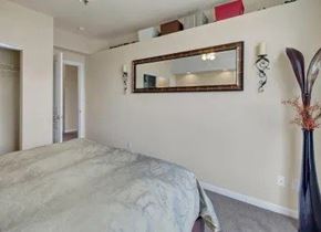 Anchorage apartment for rent - A cozy bedroom here at Park Plaza II with soft neutral carpeting and warm beige walls, featuring a comfortable bed and a large wall mirror that reflects the space for a bright, open feel.