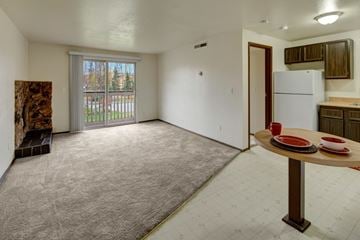 Anchorage apartment for rent - A spacious living room with a dining table and chairs, a carpeted floor, and a view of a parking lot through a sliding glass door.
