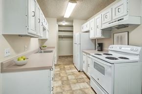 Anchorage apartment for rent - A bright and compact kitchen here at Quiet Creek with white cabinets, long neutral countertops, a white stove and refrigerator, and ample storage space under clean overhead lighting.