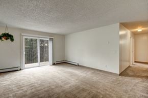Anchorage apartment for rent - A spacious, empty living room here at Quiet Creek with soft carpet, a sliding glass door that opens to a private balcony, and an open layout leading into a hallway.