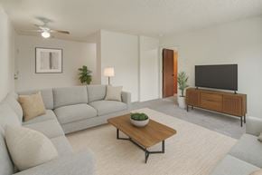 Anchorage apartment for rent - A bright living room here at Rancho Tudor with a light gray sectional sofa, a wooden coffee table, a soft neutral rug, and a modern TV console with simple greenery accents.