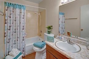 Anchorage apartment for rent - A cheerful bathroom here at Rancho Tudor with a bathtub-shower combo, an anchor-pattern shower curtain, and a marble-look vanity countertop with a bright mirror and light fixture.