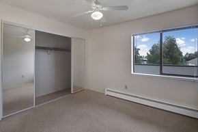 Anchorage apartment for rent - A spacious bedroom here at Silver Ridge with soft beige carpet, light walls, and a bright, airy feel. A large window brings in natural light and a view of greenery, while mirrored closet doors and a ceiling fan with light add comfort and convenience.