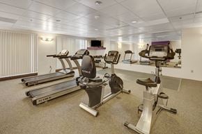 Anchorage apartment for rent - A spacious fitness center here at Susitna Ridge with treadmills, stationary bikes, and free weights, featuring carpeted flooring, bright lighting, and a large mirrored wall for an open, energizing workout space.