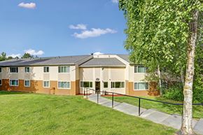 Anchorage apartment for rent - A building with a brown and beige exterior is surrounded by a green lawn and trees.