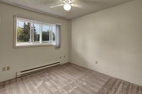 Anchorage apartment for rent - A room with a carpeted floor, a ceiling fan, and a window with a view of trees outside.