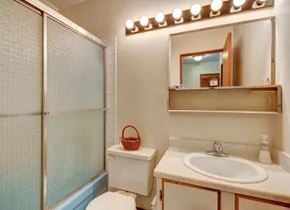 Anchorage apartment for rent - A clean bathroom at The Alaskan featuring a combination shower and tub with sliding glass doors. The vanity includes a single sink, countertop space, and a wall-mounted mirror with storage. Bright lighting, neutral walls, and simple décor complete the functional space.